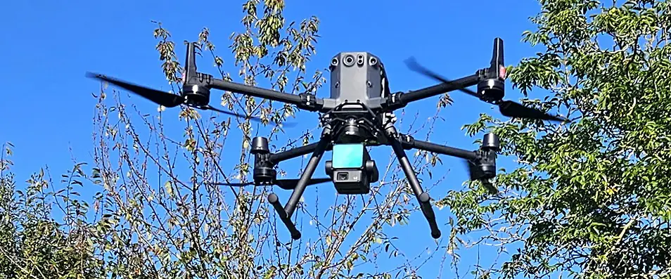 Drone DJI Matrice équipé d’un capteur laser, en vol au-dessus d’arbres, ciel bleu