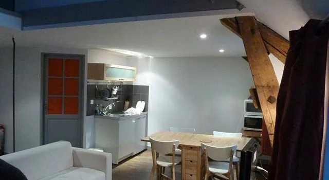 Cuisine équipée ouverte sur la salle à manger, table et chaises en bois clair, canapé
